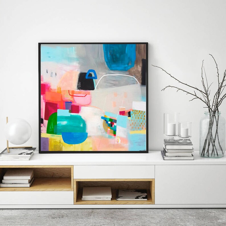 Op de afbeelding: Abstract schilderij met een kleurrijk geometrisch ontwerp. Het schilderij heeft een mix van felle kleuren, waaronder roze, blauw, groen, geel en oranje. Het schilderij is ingelijst in een zwart frame en hangt aan een witte muur.