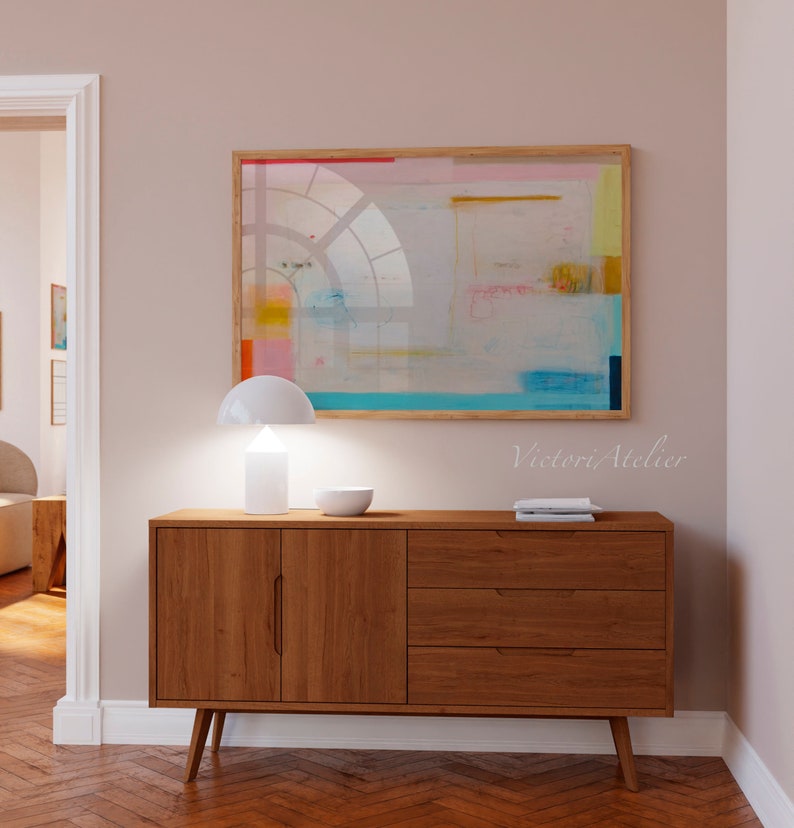 Puede incluir: Un aparador de madera de estilo moderno de mediados de siglo con dos puertas y tres cajones. Una l&aacute;mpara blanca con una pantalla blanca se coloca encima del aparador. Un cuenco blanco se coloca en el aparador junto a la l&aacute;mpara. Una pintura abstracta enmarcada con colores rosa, amarillo, azul y verde cuelga de la pared sobre el aparador. El texto "Victori Atelier" est&aacute; impreso en la pared debajo de la pintura.