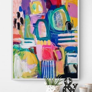 May include: Abstract painting with bold strokes of pink, yellow, blue, green, and black. The painting is framed in a white frame and is hanging on a white wall.