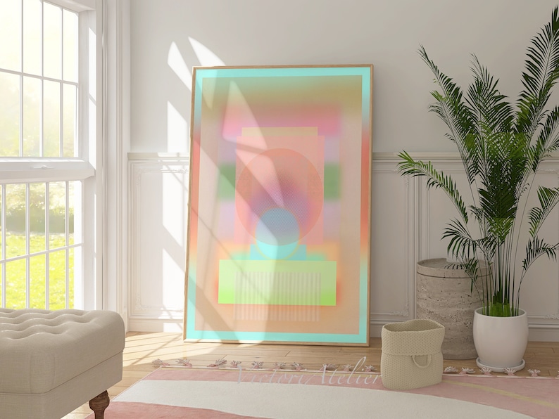 May include: Abstract art print in a light wood frame with a gradient of pink, orange, yellow, and blue colors. The print features geometric shapes and a circle in the center.