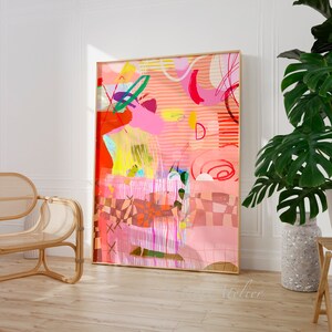 Op de afbeelding: Abstracte kunstprint met een roze, rood, oranje, geel en groen kleurenschema. De print bevat geometrische vormen, lijnen en swirls. De print is ingelijst in een gouden lijst en hangt aan een witte muur.