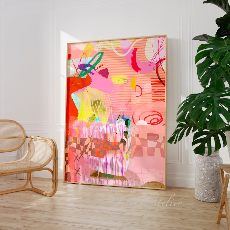 Op de afbeelding: Abstracte kunstprint met een roze, rood, oranje, geel en groen kleurenschema. De print bevat geometrische vormen, lijnen en swirls. De print is ingelijst in een gouden lijst en hangt aan een witte muur.