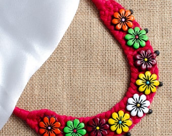 May include: A red crocheted necklace with colorful flower-shaped beads. The beads are red, green, yellow, white, and orange.