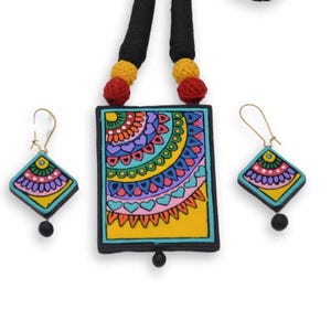 Puede incluir: Un conjunto de collar y pendientes hechos a mano, coloridos y de dise&ntilde;o geom&eacute;trico. El collar presenta un colgante rectangular con fondo amarillo y un patr&oacute;n azul, verde, rosa y morado. Los pendientes son de forma de diamante con un patr&oacute;n similar.
