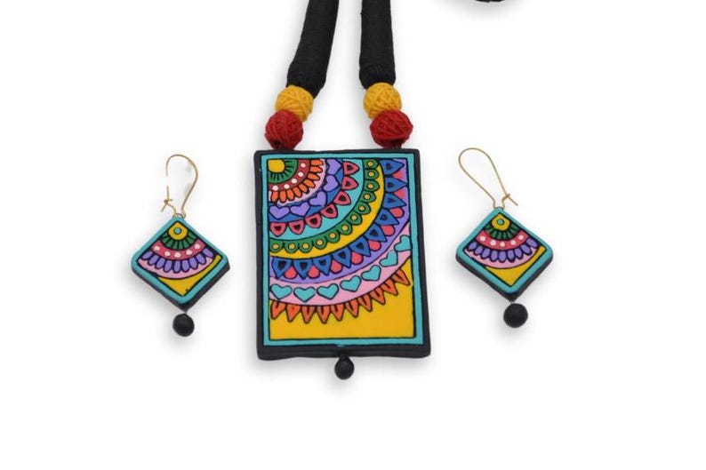 Puede incluir: Un conjunto de collar y pendientes hechos a mano, coloridos y de dise&ntilde;o geom&eacute;trico. El collar presenta un colgante rectangular con fondo amarillo y un patr&oacute;n azul, verde, rosa y morado. Los pendientes son de forma de diamante con un patr&oacute;n similar.
