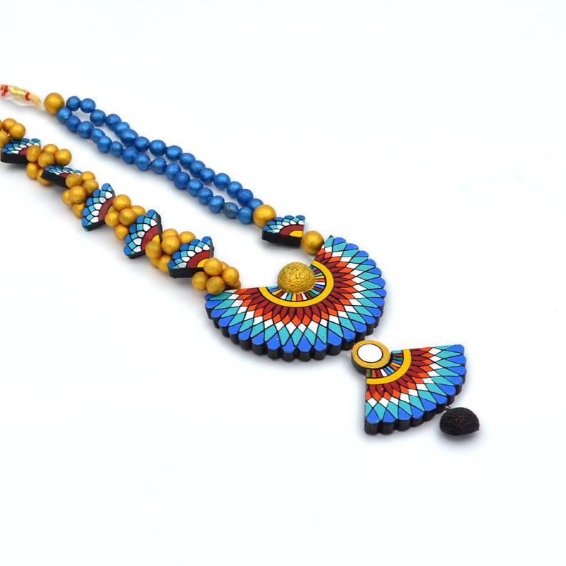 May include: A blue and gold beaded necklace with a large, colorful pendant featuring a geometric design. The pendant is shaped like a crescent moon and has a smaller, matching pendant hanging from it.