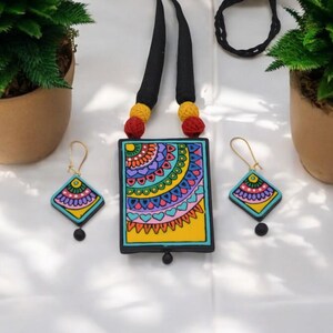 Puede incluir: Un conjunto de collar y pendientes de arcilla de colores. El collar presenta un colgante rectangular con un dise&ntilde;o de mandala azul, verde, amarillo, rosa y morado. Los pendientes son peque&ntilde;os y cuadrados con un dise&ntilde;o de mandala similar.