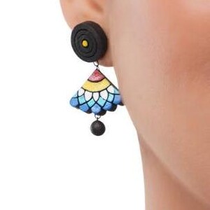 May include: A pair of black and colorful clay earrings. The earrings feature a round black top with a small yellow circle in the center, and a dangling triangular piece with a blue, white, yellow, and red design.