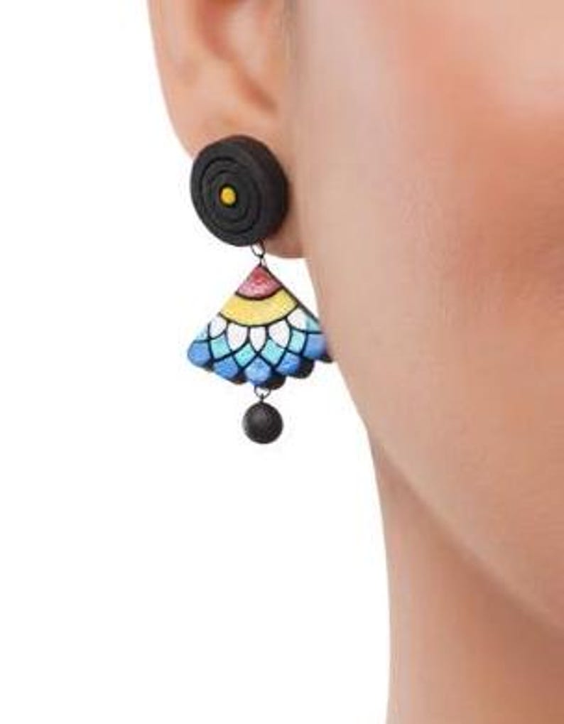 May include: A pair of black and colorful clay earrings. The earrings feature a round black top with a small yellow circle in the center, and a dangling triangular piece with a blue, white, yellow, and red design.