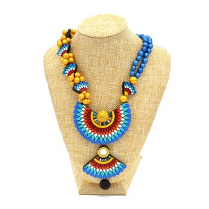 May include: A multi-strand necklace with blue and gold beads and a large, colorful pendant with a geometric design. The pendant is made of painted wood and features blue, red, white, and yellow colors.