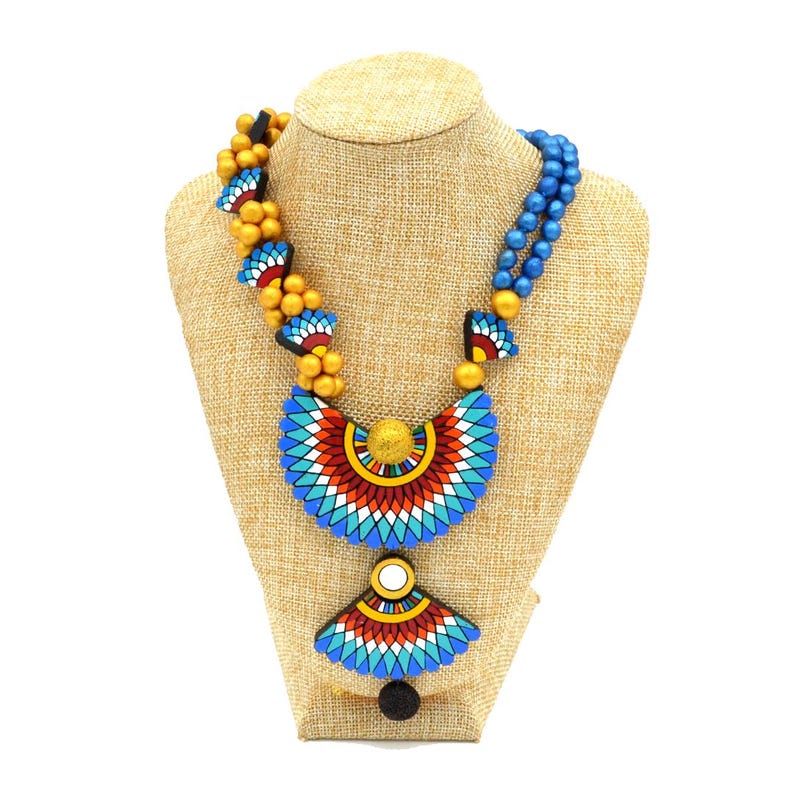 May include: A multi-strand necklace with blue and gold beads and a large, colorful pendant with a geometric design. The pendant is made of painted wood and features blue, red, white, and yellow colors.