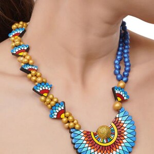 May include: A blue and gold necklace with a large, colorful pendant. The pendant is made of clay and features a geometric design. The necklace is paired with matching earrings.