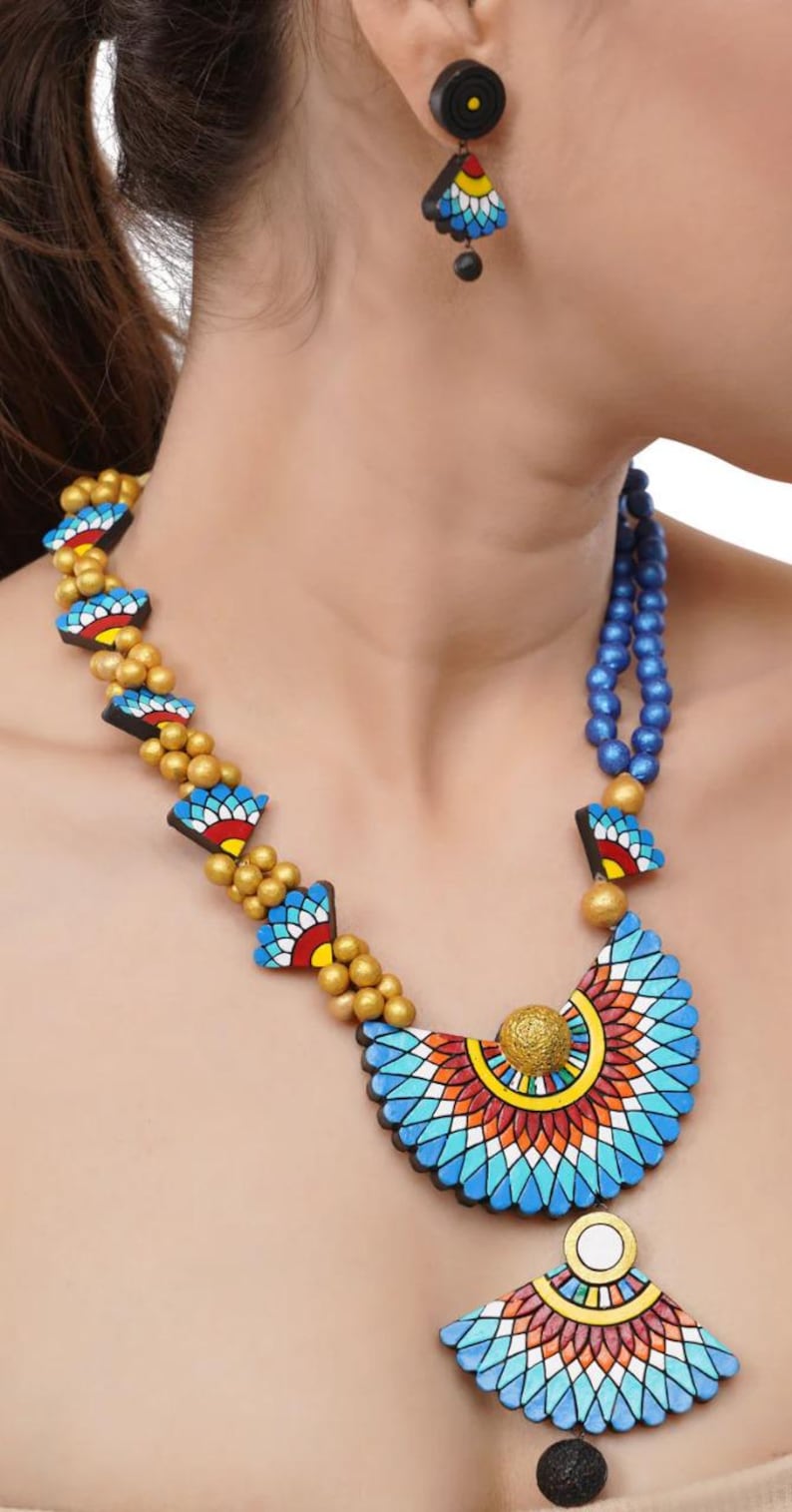 May include: A blue and gold necklace with a large, colorful pendant. The pendant is made of clay and features a geometric design. The necklace is paired with matching earrings.
