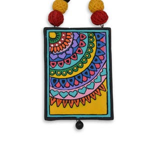 Puede incluir: Un colgante de cer&aacute;mica pintado a mano con un dise&ntilde;o geom&eacute;trico que presenta c&iacute;rculos, corazones y tri&aacute;ngulos. El colgante es amarillo, azul, verde, rosa, naranja y rojo.