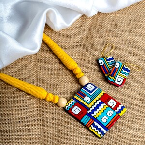 Puede incluir: Un conjunto de collar y pendientes hechos a mano. El collar presenta un cord&oacute;n amarillo con un colgante geom&eacute;trico en rojo, azul, amarillo y blanco. Los pendientes a juego tienen un dise&ntilde;o similar. El conjunto de joyas se muestra sobre una superficie texturizada.