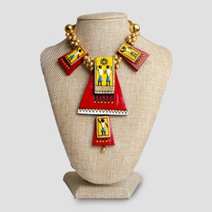 May include: A red, yellow, and blue necklace with geometric shapes and figures. The necklace is on a fabric-covered mannequin bust.