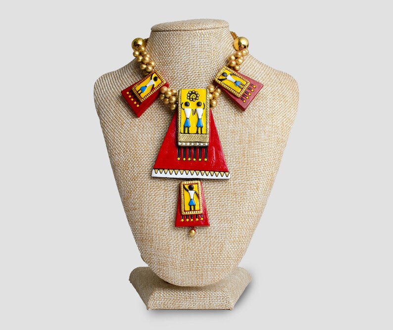 May include: A red, yellow, and blue necklace with geometric shapes and figures. The necklace is on a fabric-covered mannequin bust.