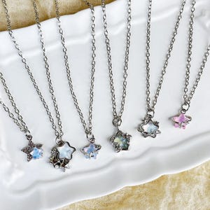 May include: Six silver necklaces with star-shaped pendants. The stars are made of iridescent glass and have a silver metal frame. Some of the stars have a small silver orb around them.