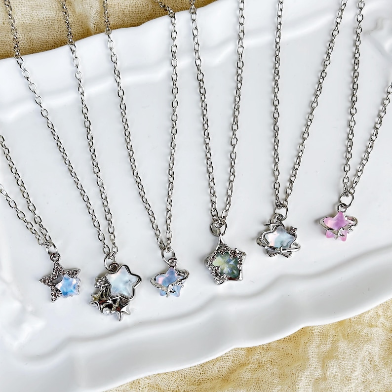 May include: Six silver necklaces with star-shaped pendants. The stars are made of iridescent glass and have a silver metal frame. Some of the stars have a small silver orb around them.
