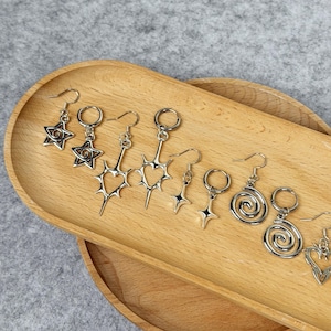 May include: A collection of silver-toned earrings displayed on a wooden tray. The earrings feature various designs, including stars, hearts, and spiral shapes. Each earring has a hook for easy wear.