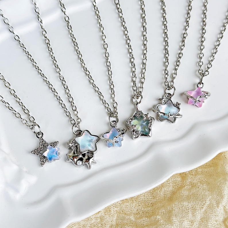 May include: Six silver necklaces with star-shaped pendants. The stars are iridescent and have a galaxy design. Some of the stars have a small planet orbiting around them.