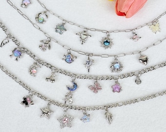 May include: Silver charm necklaces with celestial and nature-inspired pendants. The charms include stars, moons, planets, butterflies, and flowers. The necklaces are displayed on a white surface with a pink and yellow flower bouquet.