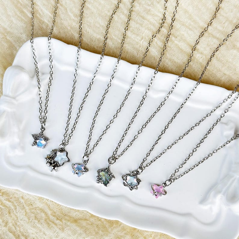 May include: A set of seven silver necklaces with different star and butterfly charms. The charms are made of iridescent glass and metal.