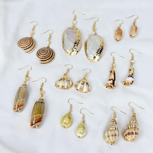 Peut inclure: Une collection de boucles d'oreilles en coquillages avec des crochets et des accents dorés. Les boucles d'oreilles présentent diverses formes de coquillages, notamment des spirales, des ovales et des motifs en éventail. Certaines coquilles ont des bords dorés et des petites perles.
