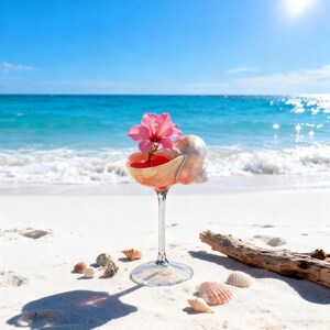 May include: A cocktail in a unique glass, with a seashell bowl and a pink flower garnish, sits on a sandy beach. The drink is a vibrant red color. Several seashells are scattered around the base of the glass, with the ocean in the background.