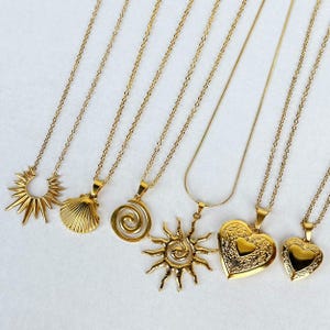Könnte beinhalten: Sechs goldene Halsketten mit verschiedenen Anhängern. Die Anhänger umfassen eine Sonne, eine Muschel, eine Spirale, ein Herzmedaillon und eine Sonne mit einer Spirale.