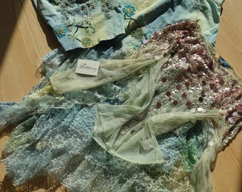 May include: A light blue denim corset top with floral beadwork, a matching denim skirt, and a layered skirt featuring light green lace, iridescent sequins, and a sheer fabric overlay. A small white tag with the text "Bikbok" is attached to the fabric.