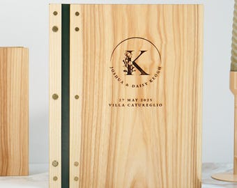 May include: Two wooden wedding menu covers with a light wood grain. Each cover has a dark green spine and brass-colored rivets. The covers are engraved with a circular design featuring the couple's initials, names, and wedding date.
