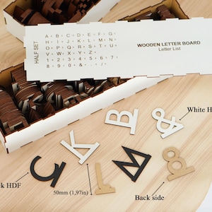 K&ouml;nnte beinhalten: Ein Holzbuchstaben-Set mit einer wei&szlig;en F&uuml;hrungskarte, die eine Alphabet- und Zahlenliste enth&auml;lt. Das Set umfasst verschiedene Buchstaben und Symbole in Schwarz, Wei&szlig; und Naturholz, aufbewahrt in einer wei&szlig;en Box. Ein Etikett zeigt 50mm an.