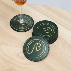May include: A set of six green leather coasters with gold stitching and the initials "AB" in gold lettering.