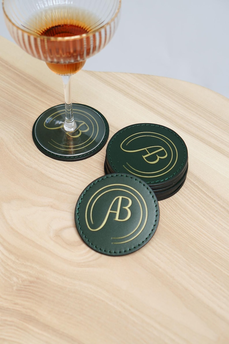 May include: A set of six green leather coasters with gold stitching and the initials "AB" in gold lettering.
