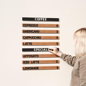 May include: A wall-mounted menu board featuring horizontal wooden slats with black lettering. The board displays coffee options like Espresso, Americano, Cappuccino, and Latte, along with a Specials section listing Affogato, Iced Latte, and Lemonade.