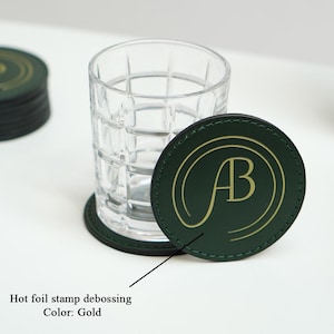 May include: Green leather coasters with a gold foil stamped debossed "AB" logo. The coasters are stacked on top of each other.