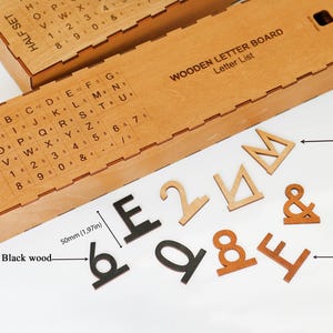 K&ouml;nnte beinhalten: Eine h&ouml;lzerne Aufbewahrungsbox f&uuml;r ein Buchstabenbrett mit aufgedruckter Buchstabenliste und einem Set aus einzelnen Buchstaben, Zahlen und Symbolen aus schwarzem, braunem und naturfarbenem Holz. Eine Ma&szlig;angabe zeigt eine H&ouml;he von 50 mm.