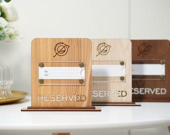 May include: Three wooden RESERVED table signs in varying shades of brown. Each sign features a clear acrylic panel for inserting a name card, and the Sparrow logo. The signs are on a white table.