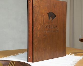 May include: A wooden menu cover with a brown leather spine. The cover has a horse silhouette and the text "MILEA" and "Steakhouse" engraved on it.