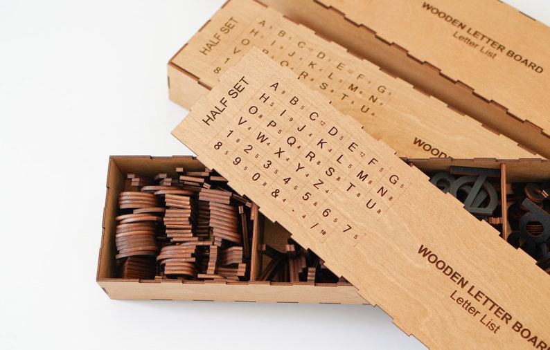K&ouml;nnte beinhalten: Eine rechteckige Aufbewahrungsbox aus Holz mit Trennw&auml;nden, die zahlreiche kleine, dunkelbraune Holzbuchstaben und Zahlen enth&auml;lt. Ein schiebbarer Holzdeckel liegt oben auf und zeigt ein aufgedrucktes Raster mit der Beschriftung HALF SET.