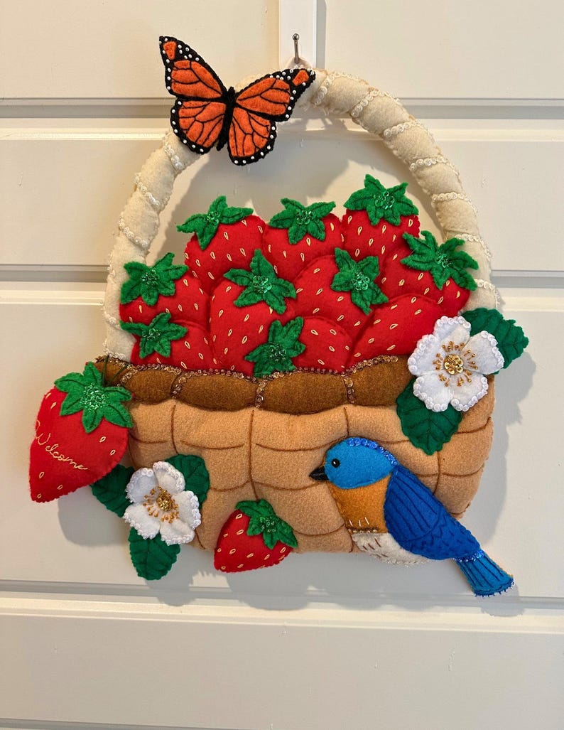 Puede incluir: Decoraci&oacute;n de cesta de fresas de fieltro con asa color crema, llena de fresas rojas y hojas verdes. Se adjuntan una mariposa monarca y un p&aacute;jaro azul. La palabra "Welcome" est&aacute; en una fresa.