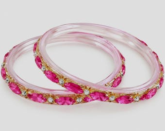 May include: Two translucent light pink bangles featuring a gold-toned band embedded with alternating marquise-cut fuchsia pink stones and small round clear white crystals arranged in a repeating pattern around the entire circumference.