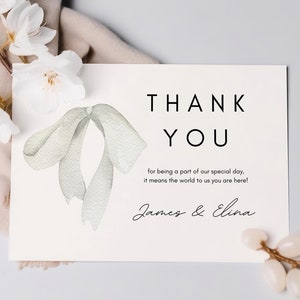 May include: A white thank you card with a watercolor illustration of a bow. The text on the card reads "THANK YOU" and "for being a part of our special day, it means the world to us you are here! James & Elina".