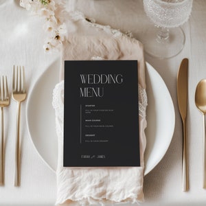 Peut inclure: Une carte de menu de mariage noire avec du texte blanc sur un couvert de table avec une assiette blanche, des couverts en or et un verre d'eau. La carte de menu indique "Wedding Menu" et comprend les titres "Starter", "Main Course" et "Dessert". La carte est signée "Farah & James".