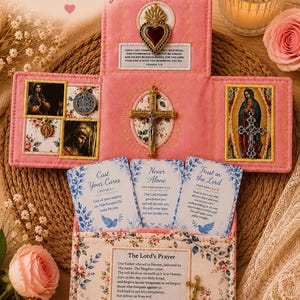 May include: A pink fabric devotional display featuring a central cross, a heart emblem, and religious imagery. It includes cards with scripture verses, a printed Lord's Prayer, and small metal charms. The text reads: A Faith-Filled Comfort Gift for Hard Days, Stress & Worry, and A little reminder that God is near, and you are never alone.