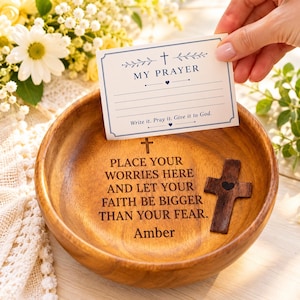 Puede incluir: Un cuenco de madera redondo grabado con el texto "PLACE YOUR WORRIES HERE AND LET YOUR FAITH BE BIGGER THAN YOUR FEAR. Amber" y una pequeña cruz. Una tarjeta titulada "MY PRAYER" con líneas para escribir se sostiene sobre el cuenco.