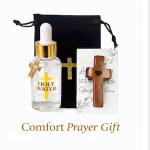 May include: A comfort prayer gift set featuring a bottle of holy water with a gold cross charm, a wooden cross, and a black drawstring bag. The bottle has a gold cap and the words "Holy Water" in yellow.