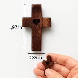 May include: A dark brown wooden pocket prayer cross with a heart-shaped cutout. The cross is 1.97 inches tall and 0.39 inches wide. The text "Pocket Prayer Cross" is at the top of the image.