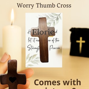 May include: A wooden pocket cross with a heart cutout, displayed with a card and a small black bag. The cross is dark brown and has the word "Eloried" on it. The text "Comes with scripture & GIFT READY" is also visible.